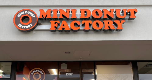 Sign for "Mini Donut Factory" in bold orange letters on a storefront.