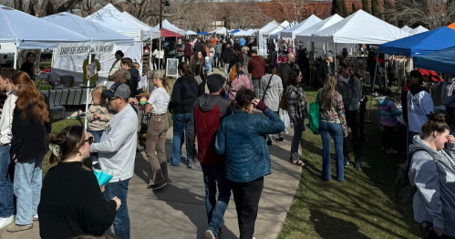 A bustling outdoor market with numerous tents and crowds of people browsing and shopping.