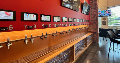 A bar with multiple beer taps, digital screens displaying options, and a modern interior design.