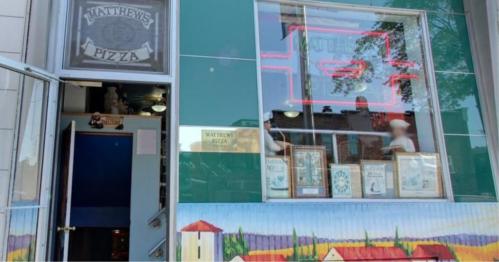Exterior of Matthew's Pizza, featuring a colorful mural and a neon sign, with people visible inside.
