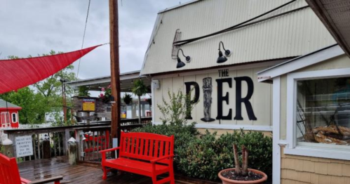 A wooden deck with a red bench in front of a building featuring a large sign that reads "The Pier." Overcast sky.