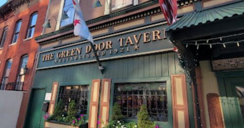 Exterior of The Green Door Tavern, established in 1921, featuring a green facade and decorative flags.