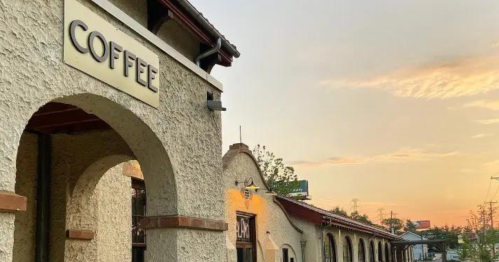 A coffee shop with a sign, set against a sunset sky and rustic architecture.