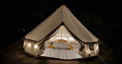 A cozy glamping tent at night, featuring a comfortable interior with soft lighting and a patterned rug.