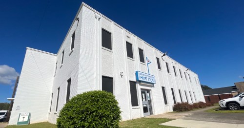 A white brick building with a sign reading "Thrift Store" and large windows under a clear blue sky.