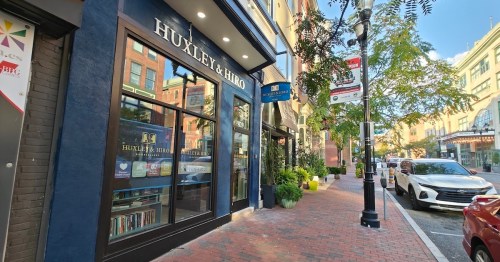 A street view of a storefront named "Huxley & Hiro," with trees and parked cars along a brick sidewalk.