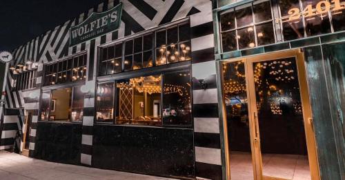 Exterior of Wolfie's, a vibrant bar with striped walls and large windows, featuring warm lighting and a welcoming entrance.