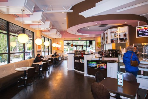 A modern café interior with seating, a counter, and large windows, featuring colorful decor and a welcoming atmosphere.