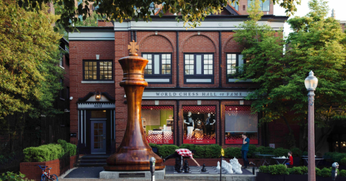 Exterior of the World Chess Hall of Fame, featuring a large wooden chess piece in front and lush greenery.