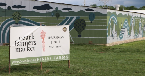 Sign for Ozark Farmers Market at Finley Farms, featuring a colorful mural and green grass in the background.