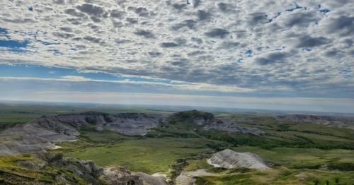 A panoramic view of rolling hills and valleys under a cloudy sky, showcasing lush greenery and rugged terrain.
