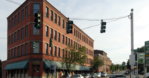 Historic brick building at an intersection with traffic lights and parked cars, set against a clear sky.