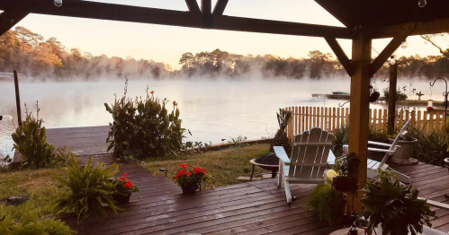 A serene lakeside view at dawn, with mist rising over the water and plants surrounding a wooden deck.