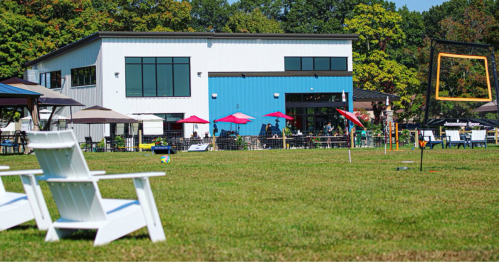 A modern building with large windows and colorful umbrellas, surrounded by green grass and outdoor seating.