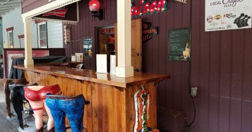 A rustic saloon bar with wooden counter and quirky stools shaped like cow legs and jeans.