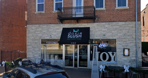 Exterior of Doxie Slush, a dessert shop, featuring a large sign and an open door, with a car parked outside.