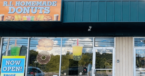 Storefront of "R.I. Homemade Donuts" featuring colorful signage, drinks, and a large donut in the window. "Now Open!" sign displayed.