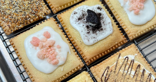 A tray of decorated pastries with various toppings, including icing, sprinkles, and crushed cookies.