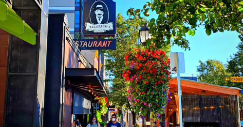 A street view of Talarico's Restaurant with colorful hanging flowers and people walking by on a sunny day.