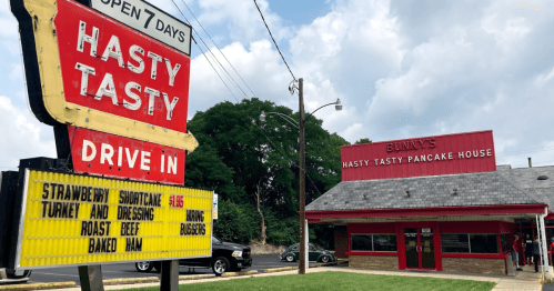 Sign for Hasty Tasty Pancake House with menu items listed, featuring a retro drive-in style building. Open 7 days.