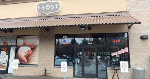 Exterior of a shop named "Frost," featuring a large glass entrance and an "Open" sign. Parking signs visible.