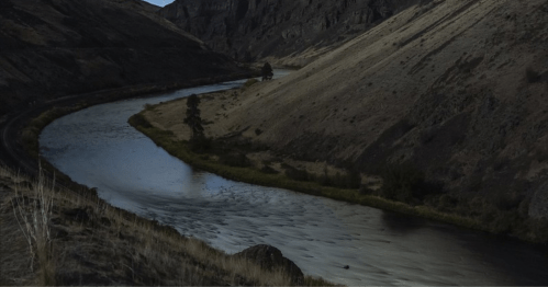 A winding river flows through a rugged landscape of hills and sparse vegetation under a clear sky.
