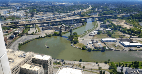 Aerial view of a river winding through an industrial area with bridges and greenery in the background.