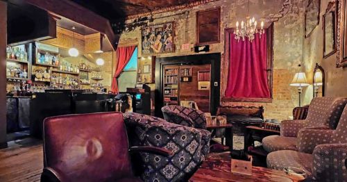 Cozy, vintage bar interior with plush seating, a well-stocked bar, and warm lighting, featuring exposed brick and rich decor.