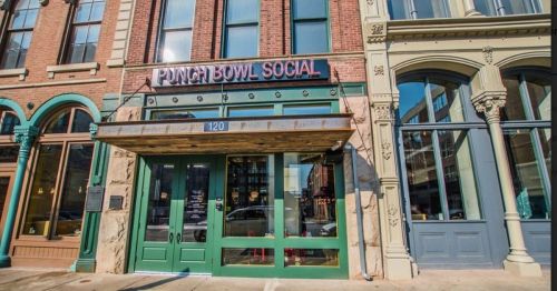 Exterior of Punch Bowl Social, featuring a green entrance and brick facade, with large windows and decorative details.