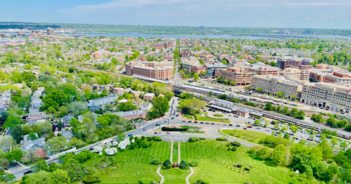 Aerial view of a vibrant cityscape with greenery, buildings, and roads under a clear blue sky.