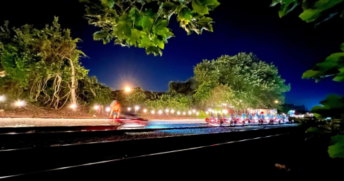 A nighttime scene of go-karts racing along a track, illuminated by lights and surrounded by greenery.