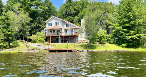A serene lakeside house surrounded by trees, featuring a deck and a calm water view.