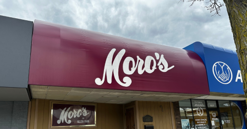 Sign for "Moro's" restaurant with a maroon awning, located in a commercial area under a cloudy sky.