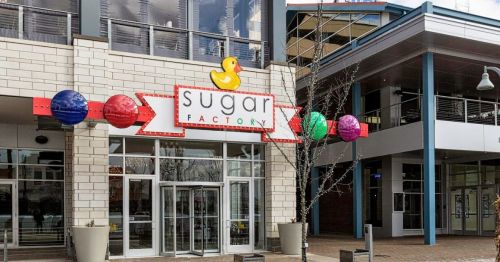 Exterior of Sugar Factory restaurant, featuring a colorful sign with a duck logo and vibrant decorative spheres.