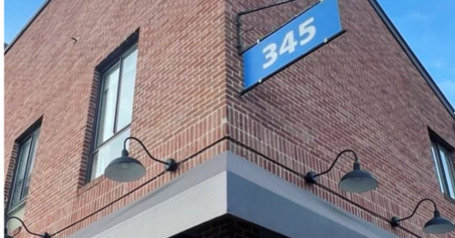 Corner of a brick building with a blue sign displaying the number 345 and wall-mounted lights.