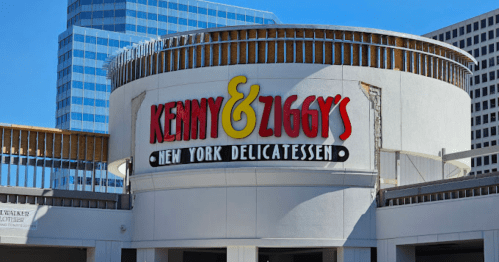 Sign for Kenny & Ziggy's New York Delicatessen on a building, with a clear blue sky in the background.