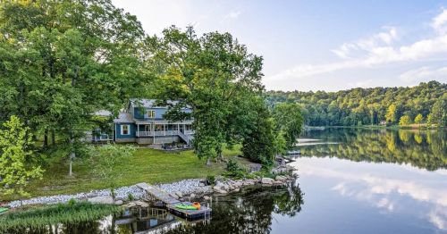 A serene lakeside view featuring a house surrounded by trees, with a calm water reflection and a small dock.