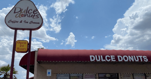 Sign for Dulce Donuts, featuring "Open 24 Hours" and a storefront with a red awning under a cloudy sky.