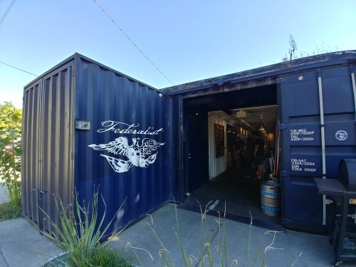 A blue shipping container with "Federalist" and an eagle logo, leading to a lively entrance with people inside.