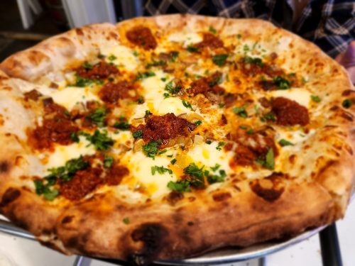 A close-up of a freshly baked pizza topped with cheese, herbs, and spicy sausage on a golden crust.