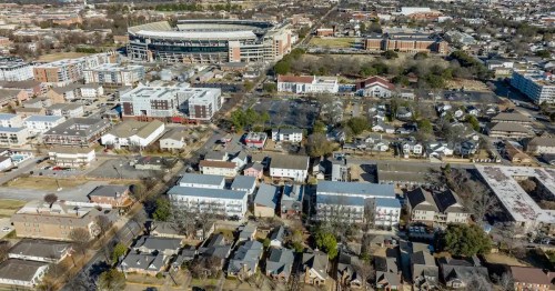 Aerial view of a cityscape featuring residential areas, commercial buildings, and a large stadium in the background.