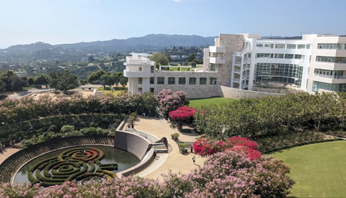 A scenic view of a modern building surrounded by lush gardens and colorful flowers, with mountains in the background.