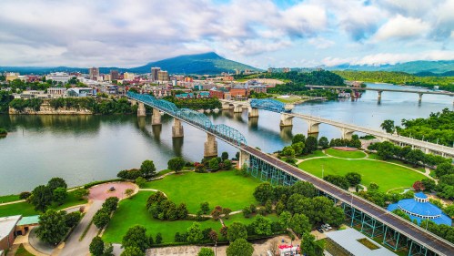 Aerial view of Chattanooga, Tennessee, featuring bridges over a river and lush green parks along the waterfront.