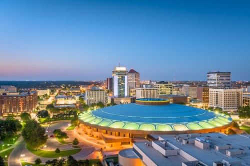 Aerial view of a city skyline at dusk, featuring a circular building with a green roof and surrounding urban landscape.