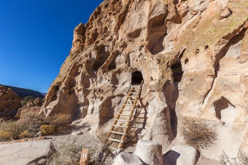A rocky cliff with a wooden ladder leading to cave-like openings under a clear blue sky.