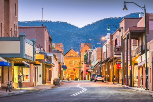 A quiet street scene with shops, mountains in the background, and a historic building at the end of the road.