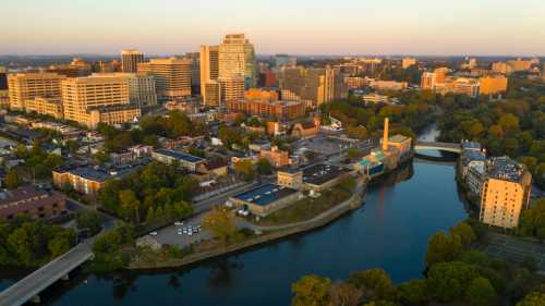 Aerial view of a city skyline with buildings, trees, and a river at sunset.