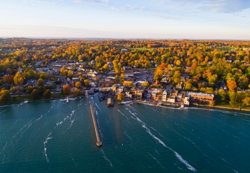 Aerial view of a waterfront town surrounded by colorful autumn trees and a calm river.