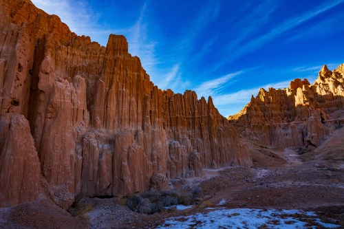 A dramatic landscape of towering red rock formations under a blue sky with wispy clouds.