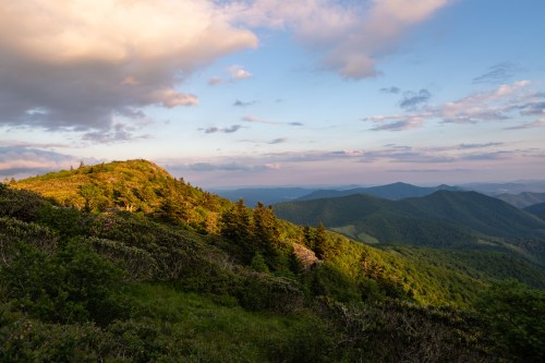 A scenic view of rolling green mountains under a partly cloudy sky during sunset.
